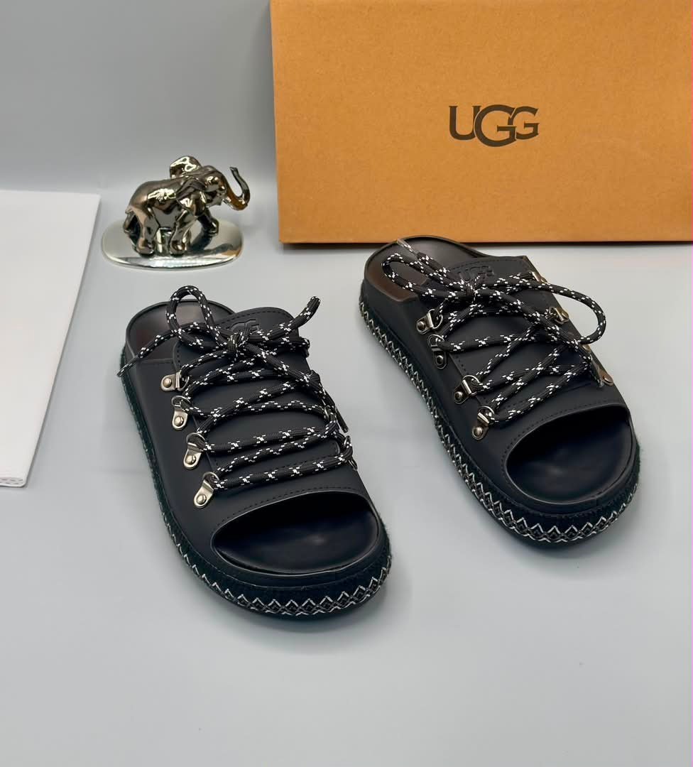 root-OZV1AT.jpeg Black Leather UGG Slide Sandals with Silver Laces and Stitching - Image 1