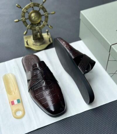 A pair of luxurious black leather half shoes displayed on a white surface, accompanied by a small Italian flag and a decorative gold ship's wheel, exuding elegance and refinement.