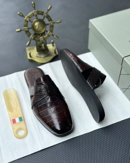 A pair of luxurious black leather half shoes displayed on a white surface, accompanied by a small Italian flag and a decorative gold ship's wheel, exuding elegance and refinement.