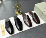 A pair of luxurious black leather half shoes displayed on a white surface, accompanied by a small Italian flag and a decorative gold ship's wheel, exuding elegance and refinement.