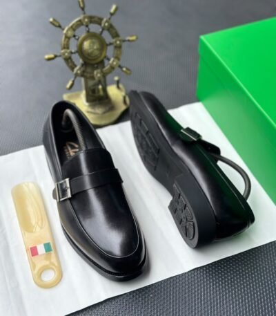 A pair of luxurious black leather loafers with a sleek design and sophisticated buckle, presented on a crisp white surface with a touch of Italian flair.