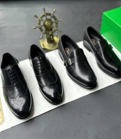 A pair of luxurious black leather oxfords showcased on a crisp white surface, accompanied by a shoe tree and a green box, exuding an air of sophistication.