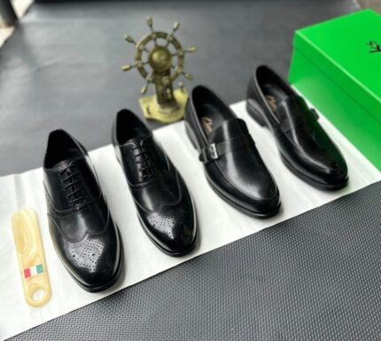 A pair of luxurious black leather oxfords showcased on a crisp white surface, accompanied by a shoe tree and a green box, exuding an air of sophistication.