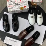 A luxurious display of Dolce & Gabbana half shoes in black, brown, and white, accompanied by the brand's signature box and cloth.