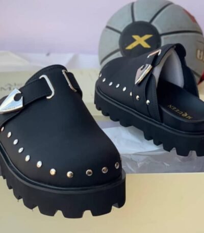 A pair of luxurious green half shoes with metallic studs and a sophisticated buckle, showcased on a cream-colored shoe box.