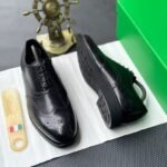 A pair of luxurious black leather oxfords showcased on a crisp white surface, accompanied by a shoe tree and a green box, exuding an air of sophistication.