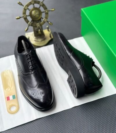 A pair of luxurious black leather oxfords showcased on a crisp white surface, accompanied by a shoe tree and a green box, exuding an air of sophistication.