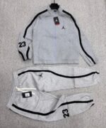A luxurious black Nike tracksuit with grey accents, laid out on a grey surface, showcasing its sleek design and iconic logo.