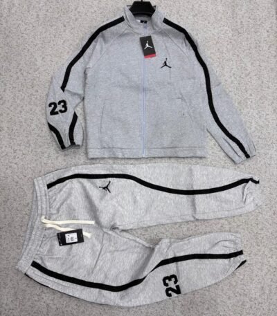A luxurious black Nike tracksuit with grey accents, laid out on a grey surface, showcasing its sleek design and iconic logo.