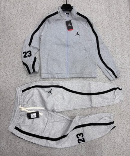 A luxurious black Nike tracksuit with grey accents, laid out on a grey surface, showcasing its sleek design and iconic logo.