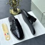 A pair of luxurious black leather half shoes displayed on a white surface, accompanied by a small Italian flag and a decorative gold ship's wheel, exuding elegance and refinement.