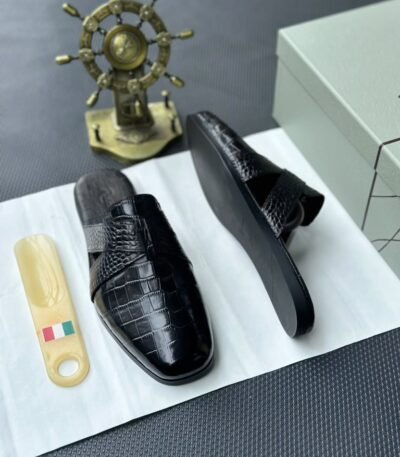 A pair of luxurious black leather half shoes displayed on a white surface, accompanied by a small Italian flag and a decorative gold ship's wheel, exuding elegance and refinement.