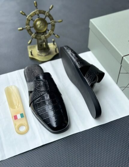 A pair of luxurious black leather half shoes displayed on a white surface, accompanied by a small Italian flag and a decorative gold ship's wheel, exuding elegance and refinement.