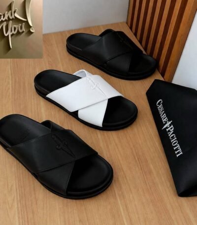 Luxurious slides in black and white, displayed on a wooden table with a black bag featuring the brand name 'Cesare Paciotti'.