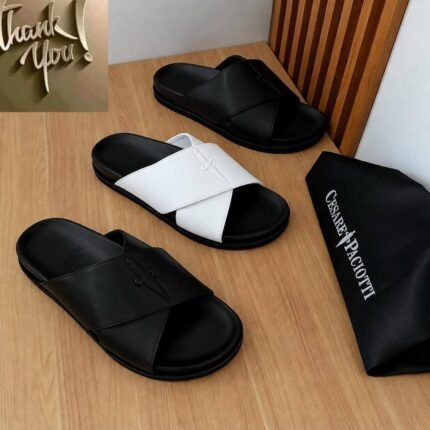 Luxurious slides in black and white, displayed on a wooden table with a black bag featuring the brand name 'Cesare Paciotti'.