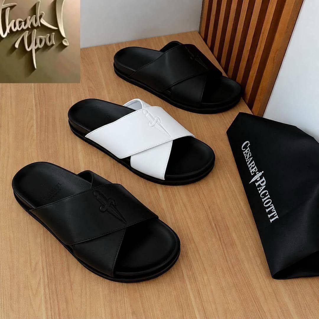 root Luxurious slides in black and white, displayed on a wooden table with a black bag featuring the brand name 'Cesare Paciotti'.