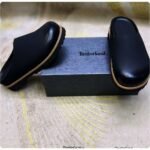 A pair of luxurious black leather half shoes with tan trim, elegantly displayed on a gray box with the Timberland logo.