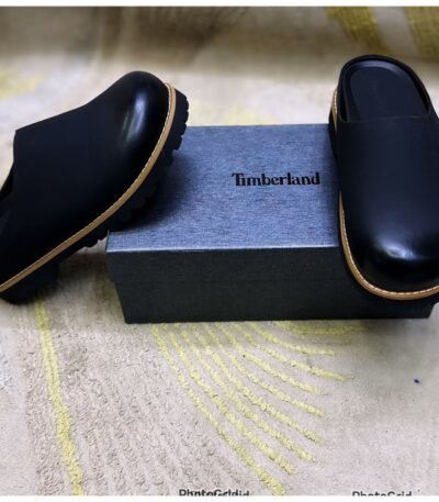 A pair of luxurious black leather half shoes with tan trim, elegantly displayed on a gray box with the Timberland logo.