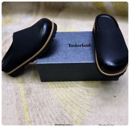 A pair of luxurious black leather half shoes with tan trim, elegantly displayed on a gray box with the Timberland logo.