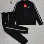 A luxurious black Nike tracksuit with grey accents, laid out on a grey surface, showcasing its sleek design and iconic logo.