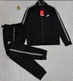A luxurious black Nike tracksuit with grey accents, laid out on a grey surface, showcasing its sleek design and iconic logo.
