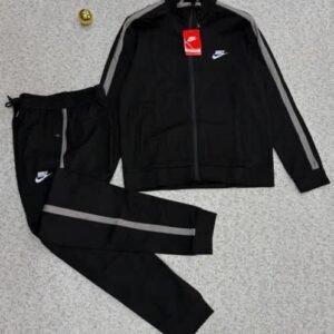 A luxurious black Nike tracksuit with grey accents, laid out on a grey surface, showcasing its sleek design and iconic logo.