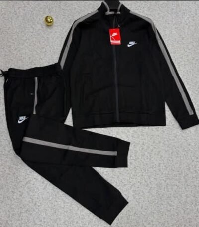 A luxurious black Nike tracksuit with grey accents, laid out on a grey surface, showcasing its sleek design and iconic logo.