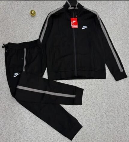 A luxurious black Nike tracksuit with grey accents, laid out on a grey surface, showcasing its sleek design and iconic logo.