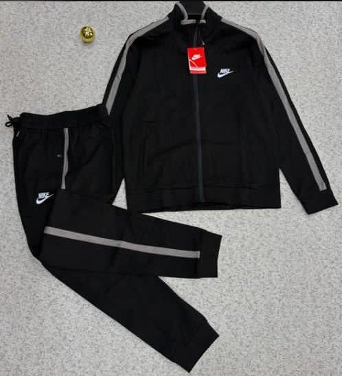 root A luxurious black Nike tracksuit with grey accents, laid out on a grey surface, showcasing its sleek design and iconic logo.