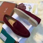 A pair of luxurious maroon loafers with velvety texture, displayed on a white shoe box with accessories and packaging in the background.